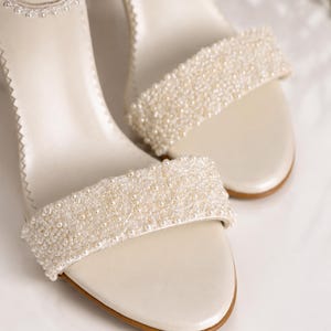 Close-up of handmade ivory pearlized leather bridal sandals featuring intricate pearl beadwork and premium craftsmanship on a clean luxury studio background.