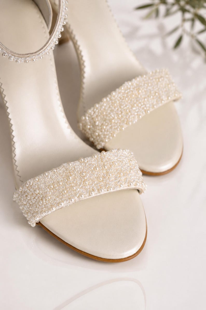 Close-up of handmade ivory pearlized leather bridal sandals featuring intricate pearl beadwork and premium craftsmanship on a clean luxury studio background.