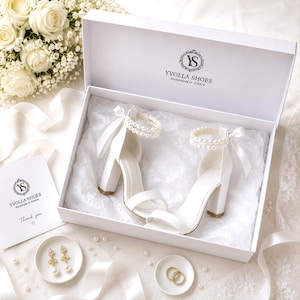 Wedding details flat lay featuring white bridal shoes, wedding rings, earrings and YvollaShoes packaging.