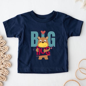 May include: A navy blue short-sleeved t-shirt with a cartoon bear holding a red sign that says "BIG HUG". The bear has brown fur, a yellow nose, and a red heart above its head.