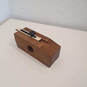 Könnte beinhalten: Ein Werkzeug aus Holz mit einem Schiebemechanismus und einem Knopf. Das Werkzeug ist auf beiden Seiten mit "15°" gekennzeichnet.