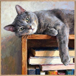 May include: A square oil painting in a light wood frame depicting a gray cat resting on top of a wooden bookshelf filled with stacked books. The cat has green eyes and is looking forward, with one paw hanging over the edge of the shelf.