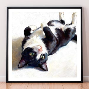 A framed oil pastel art print of a black and white tuxedo cat lying on its back with green eyes, looking up at the viewer.