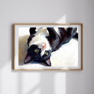 K&ouml;nnte beinhalten: Ein gerahmtes &Ouml;lgem&auml;lde einer schwarz-wei&szlig;en Katze, die auf dem R&uuml;cken liegt. Die Katze hat gr&uuml;ne Augen und schaut nach oben. Das Gem&auml;lde zeichnet sich durch sichtbare Pinselstriche und eine kontrastreiche Farbpalette aus.