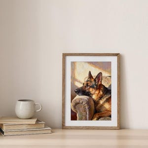 The framed German Shepherd print resting on a wooden surface beside a stack of books and a speckled mug.