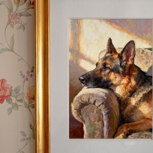 Close-up of the framed German Shepherd print in a gold frame mounted on floral wallpaper.