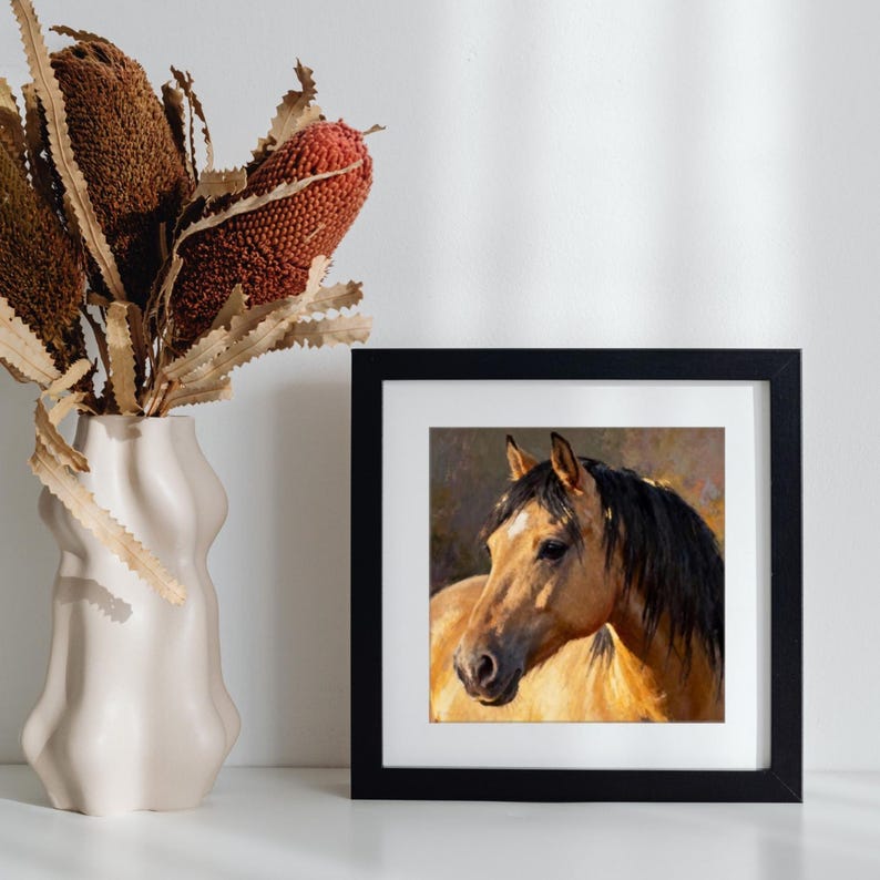 May include: A square black frame containing a painting of a tan horse with a black mane and a white star on its forehead. The horse is depicted in profile against a soft, muted background. The frame features a white mat border around the artwork.