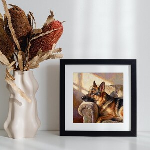 The German Shepherd print in a black frame displayed on a white shelf beside a cream-colored ceramic vase with brown dried stems.