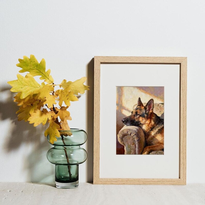A small framed print of the German Shepherd sitting next to a green glass vase holding yellow oak leaves.