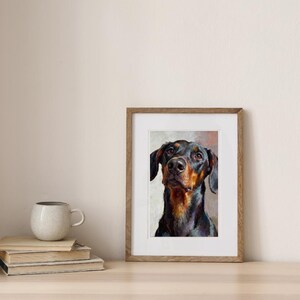 K&ouml;nnte beinhalten: Ein gerahmter &Ouml;lgem&auml;ldedruck mit dem Portr&auml;t eines Dobermanns mit schwarzem und lohfarbenem Fell. Der Hund ist von der Brust aufw&auml;rts vor einem neutralen, strukturierten Hintergrund dargestellt. Der Rahmen besteht aus hellbraunem Holz mit wei&szlig;em Passepartout.