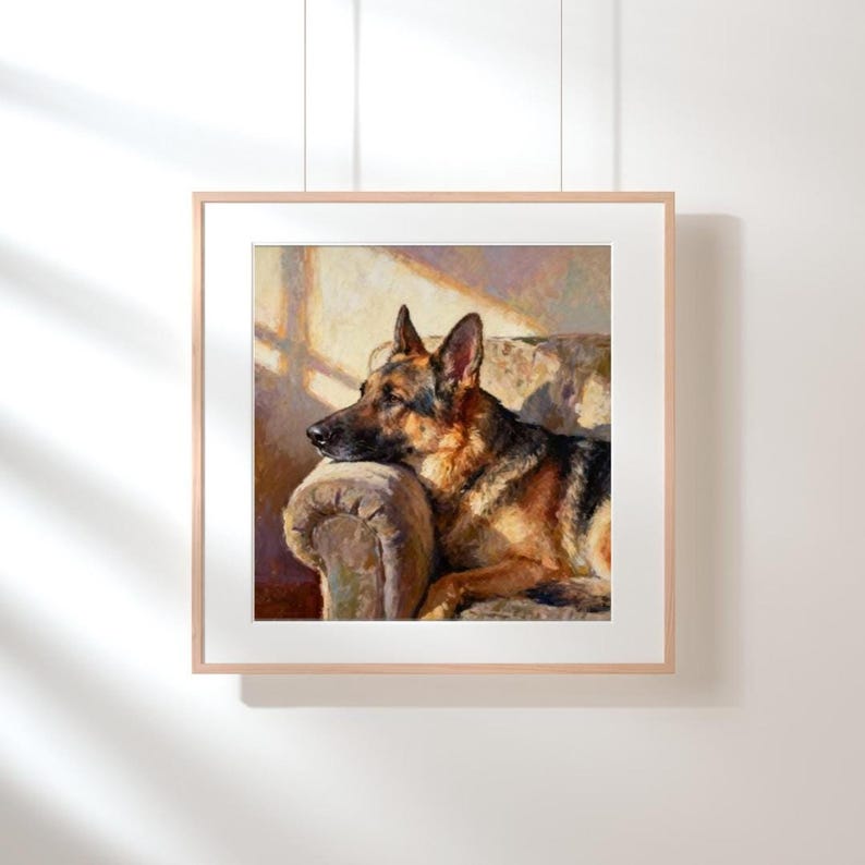A square print of a German Shepherd resting its head on an armchair, hanging in a light wood frame on a white wall.