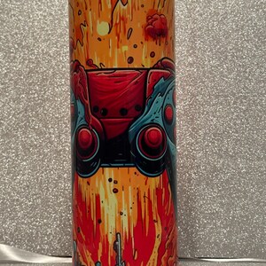 May include: A stainless steel tumbler featuring a colourful graphic of a video game controller exploding against a fiery orange and yellow background.
