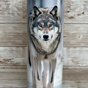 May include: A stainless steel tumbler with a wolf image. The wolf is gray and white and is standing in the snow. The tumbler is a great way to keep your drinks cold or hot.