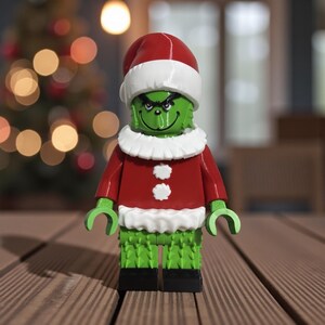May include: A green character figure wearing a red Santa suit with white trim and a matching hat. The figure has a grumpy expression and is made of interlocking plastic bricks. The figure is standing on a wooden surface.