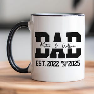 May include: White ceramic mug with a black rim and handle. The mug has black text that reads "DAD Mateo & William EST. 2022 AGAIN EST. 2025".