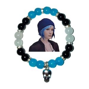 May include: A bracelet with blue, black, and white beads, with rhinestone spacers. A silver skull charm dangles from the bracelet. A digital image of a person with blue hair is in the background.