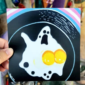 Może przedstawiać: Czarno-biała ilustracja jajka sadzonego w kształcie ducha z dwoma żółtymi żółtkami. Jajko znajduje się na czarnej patelni z białym rantem.