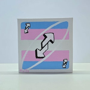Pode incluir: Uma pintura em tela quadrada com um design de carta de reversão com listras horizontais em azul claro, rosa e branco. O centro exibe um ícone de seta branca grande com contorno preto, com ícones menores correspondentes nos cantos.