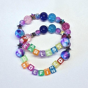 May include: Two beaded bracelets with the words "FEARLESS" and "UNDEFINED" spelled out in colorful letter beads. The bracelets feature a mix of purple, blue, and pink beads, along with star-shaped accents.