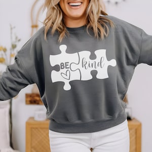May include: A gray sweatshirt with a white puzzle piece design that says "be kind" with a heart in the middle of the "be" piece.
