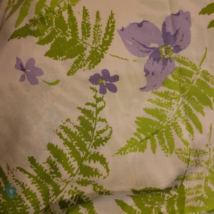 Könnte beinhalten: Ein weißer Stoff mit einem Muster aus grünen Farnen und violetten Blumen.