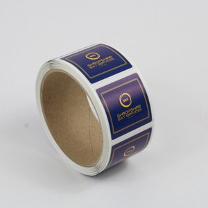 May include: A roll of square stickers with a navy blue background and gold trim. Each sticker features the text "SHROPSHIRE BAY SERVICES" and a gold circular logo. The stickers are on a white background.