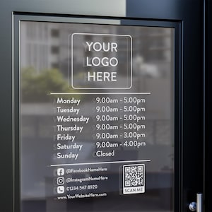 Op de afbeelding: Een wit bord met zwarte tekst op een glazen deur. Het bord heeft bovenaan de tekst "YOUR LOGO HERE", gevolgd door een dagelijks schema van openingstijden. Het bord bevat ook contactgegevens, een QR-code en de tekst "SCAN ME".