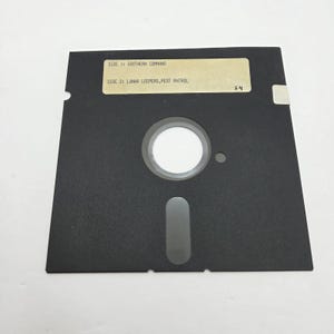 Puede incluir: Un disquete negro de 5,25 pulgadas con una etiqueta blanca. La etiqueta dice "SIDE 1: SOUTHERN COMMAND" y "SIDE 2: LUNAR LEEPERS, PEST PATROL". El disco tiene un gran agujero central y un recorte ovalado más pequeño.