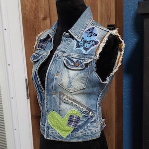 May include: A blue denim vest with a heart-shaped patch, a butterfly patch, and frayed edges.