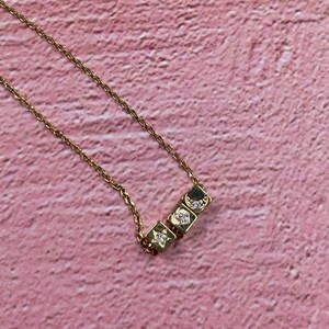 May include: A gold chain necklace with three small, square charms. Each charm has a different design: a star, a heart, and a crescent moon. The charms are adorned with small, clear crystals.