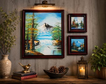 Op de afbeelding: Drie ingelijste olieverfschilderijen met berglandschappen, watervallen, dennenbomen en een blauwe lucht. De kunstwerken zijn geplaatst in donkerhouten lijsten, met één groot vierkant schilderij en twee kleinere vierkante schilderijen aan de muur.