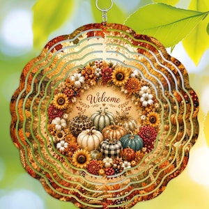 May include: A circular metal wind spinner featuring a scalloped edge and a central design of a harvest wreath with pumpkins, sunflowers, and autumn foliage. The word Welcome is printed in the center, surrounded by various patterned pumpkins.