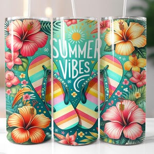 May include: A vibrant tumbler with a tropical design. It features the words "Summer Vibes" above a pair of rainbow-striped flip-flops. The tumbler is adorned with colorful hibiscus flowers and lush green foliage, perfect for summer.