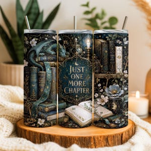 Puede incluir: Un vaso cilíndrico con pajita de metal que presenta una ilustración de fantasía oscura con libros antiguos apilados, un dragón verde, una vela encendida y un libro abierto. El texto central dice Just One More Chapter, rodeado de flores.
