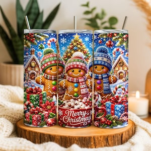 May include: A cylindrical tumbler with a straw featuring a Christmas scene with three gingerbread characters wearing colourful knit hats and scarves, surrounded by decorated gift boxes, candy canes, a lit tree, and the text Merry Christmas.
