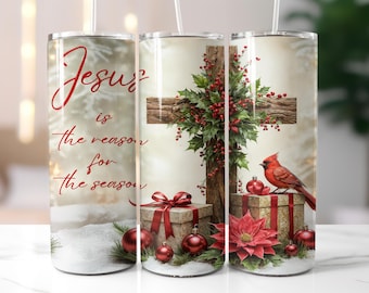 May include: A tumbler featuring a Christmas theme with the text "Jesus is the reason for the season." The design includes a wooden cross, a red cardinal, holly, gift boxes, and ornaments. The tumbler has a white straw.