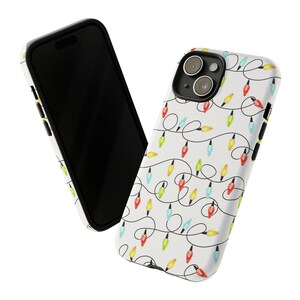 Puede incluir: Una funda de tel&eacute;fono blanca con un borde negro y un patr&oacute;n de luces navide&ntilde;as de colores. La funda tiene un recorte para el objetivo de la c&aacute;mara.