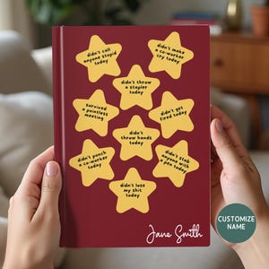 May include: A burgundy journal with gold star stickers, each with a humorous phrase. The phrases include "didn't call anyone stupid today" and "didn't lose my shit today." The journal is personalized with the name "Jane Smith."
