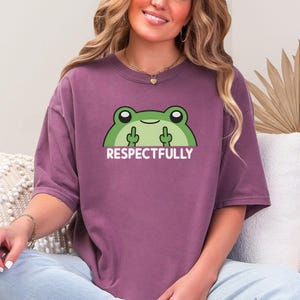 May include: Berry-colored t-shirt featuring a green cartoon frog with the text "Respectfully" and two middle fingers. The shirt is a relaxed fit and has short sleeves. The frog graphic is centered on the front of the shirt.