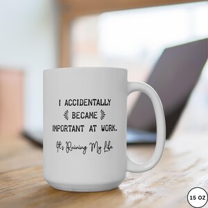 Op de afbeelding: Witte keramische mok met de tekst "I accidentally became important at work. It's Ruining My Life." De mok heeft een groot handvat en staat op een houten oppervlak. De mok is 444 ml.