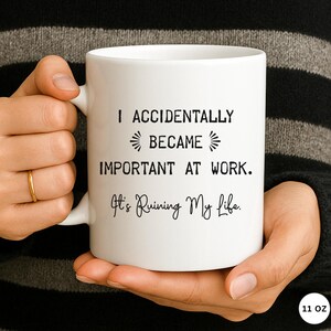 Op de afbeelding: Witte keramische mok met zwarte tekst: "I ACCIDENTALLY BECAME IMPORTANT AT WORK. It's Ruining My Life." De mok wordt door een persoon vastgehouden. De mok is 312 gram.