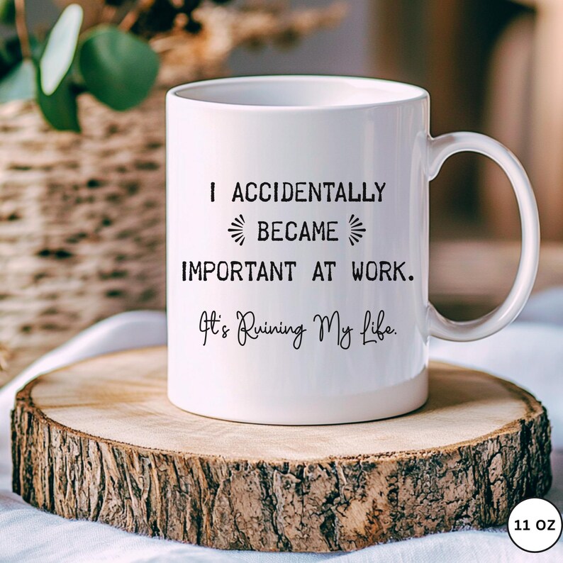 Op de afbeelding: Witte keramische mok met de tekst "I ACCIDENTALLY BECAME IMPORTANT AT WORK. It's Ruining My Life." De mok staat op een houten schijf.