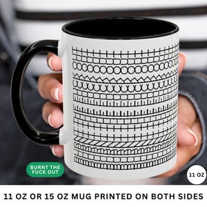 May include: White ceramic mug with a black handle and interior. The mug features a repeating black pattern of geometric shapes and the text "BURNT THE FUCK OUT". The mug is labeled as 11 oz.