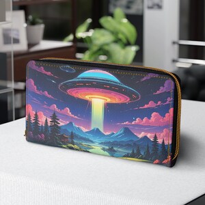May include: A black zippered wallet with a colorful graphic print of a flying saucer over a landscape with mountains and trees. The saucer is emitting a beam of light.