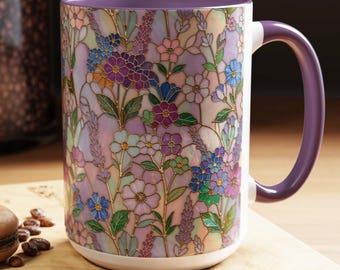 Può includere: Una grande tazza in ceramica con un motivo floreale a vetrata colorata nei toni del viola, blu e verde. La tazza ha una base bianca, un bordo viola e un manico viola. Un cucchiaio e un macaron sono su una superficie di legno.
