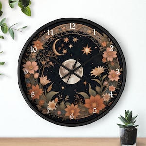 May include: A circular wall clock with a black frame. The clock face depicts a dark blue night sky with a full moon, stars, and a crescent moon. Floral and botanical elements in shades of orange and beige surround the clock face. The clock hands are black.