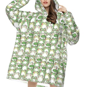 May include: A hooded blanket featuring a repeating pattern of cartoon frogs in shades of green, white, and pink. The blanket has long sleeves and a hood, offering a cozy and whimsical design. The frog pattern is consistent across the entire blanket.
