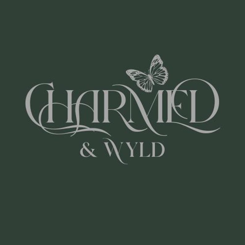 May include: A dark green background with the words "CHARMED & WYLD" in a stylized, light gray font. A detailed butterfly graphic is positioned above the letter "M" in "CHARMED". The overall design is elegant and decorative.