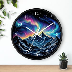 Pode incluir: Um relógio de parede redondo com moldura preta. O mostrador apresenta uma paisagem montanhosa sob um céu colorido de aurora boreal. Os ponteiros brancos indicam as horas. O relógio está sobre uma superfície de madeira.