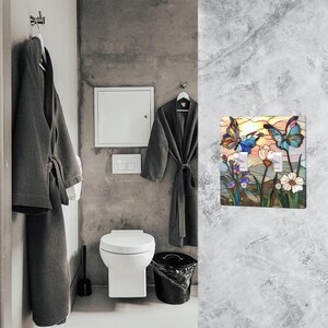 Puede incluir: Una cubierta decorativa para interruptor de luz con un dise&ntilde;o de vidriera que presenta dos mariposas, flores y una puesta de sol. La cubierta tiene dos interruptores de luz. El fondo incluye una valla blanca y flores coloridas.